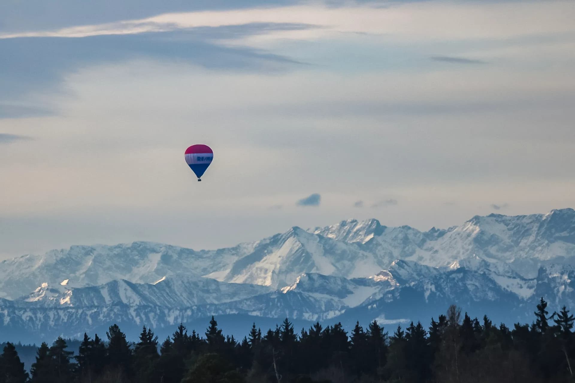 Ein Heißluftballon schwebt über der verschneiten Alpenkette