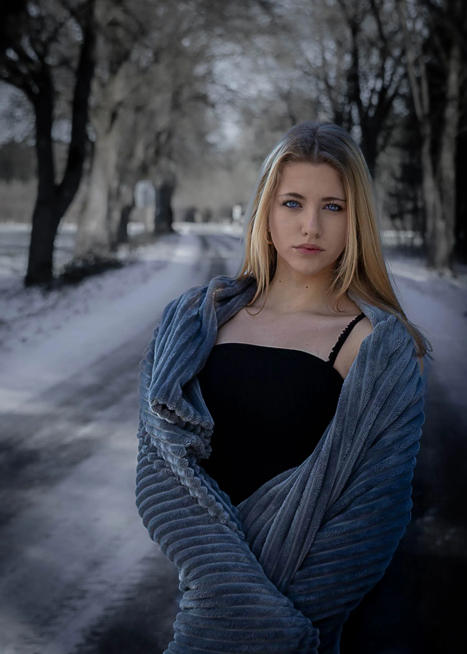 Portrait einer jungen Frau in eine Decke gehüllt auf einer winterlichen Allee